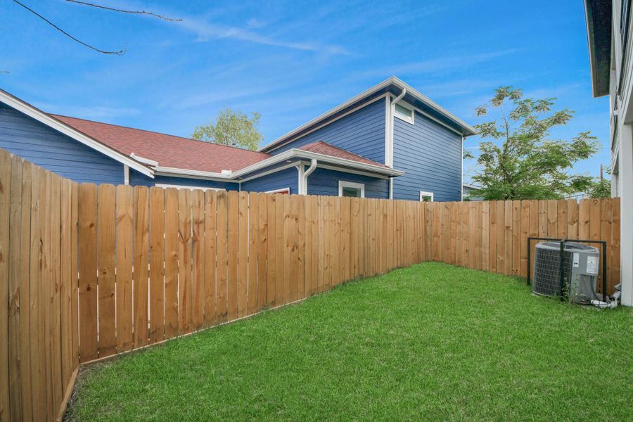 This cozy backyard offers a private retreat with lush green grass, framed by a charming wooden fence, perfect for relaxing or entertaining.