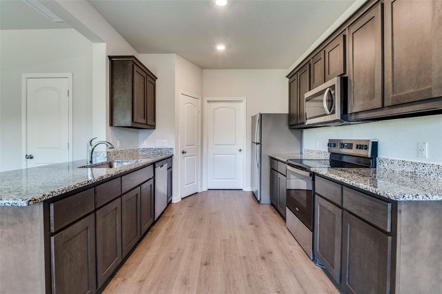 Kitchen with stainless steel appliances, dark wood finish cabinetry, light stone counters, and light wood-style floors