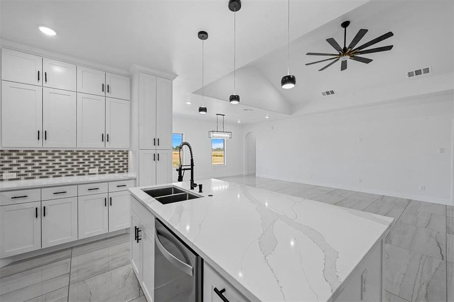 Kitchen with decorative light fixtures, dishwasher, an island with sink, sink, and lofted ceiling