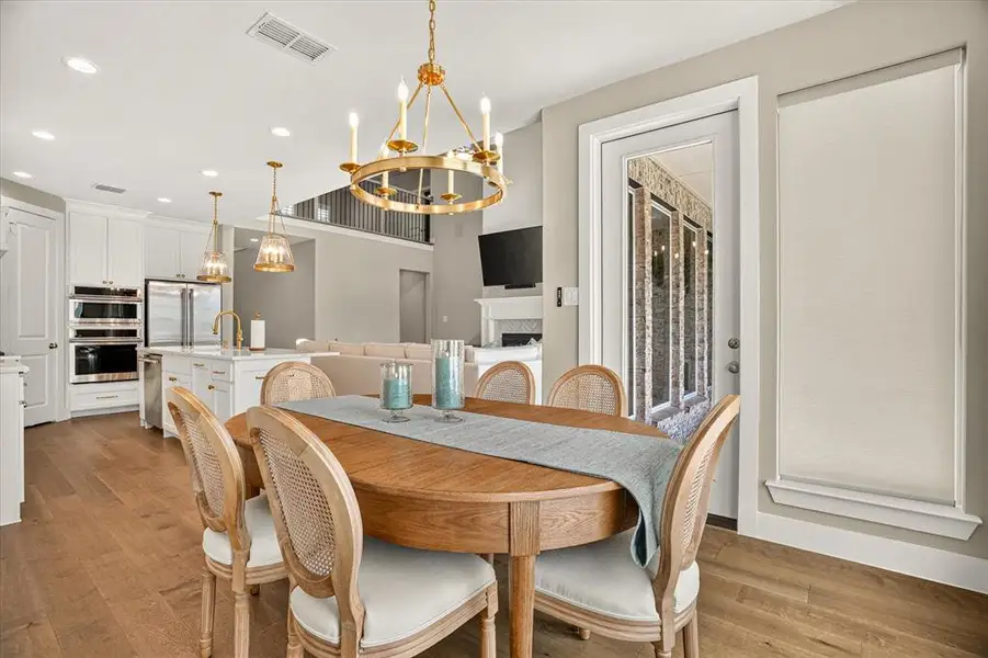 Open-concept dining area featuring wood-finish flooring, a brass chandelier, and direct access to an outdoor patio through a glass-paneled door Open-concept dining area featuring wood-finish flooring, a brass chandelier, and direct access to an outdoor patio through a glass-paneled door