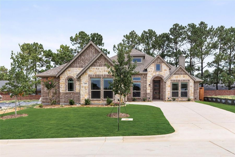 Single-story home with brick and stone exterior, arched entry, and curved driveway with green lawn