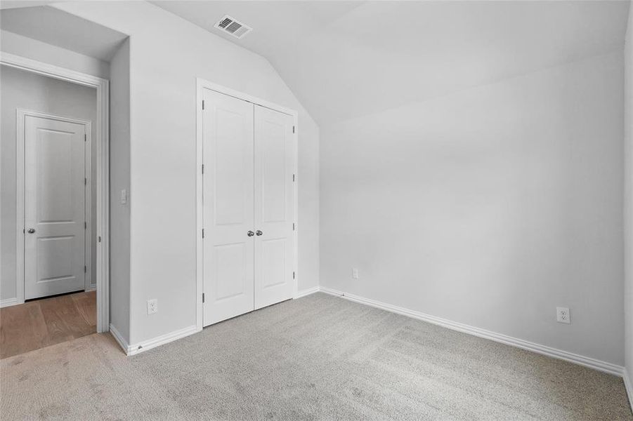 Unfurnished bedroom with vaulted ceiling, light colored carpet, and a closet