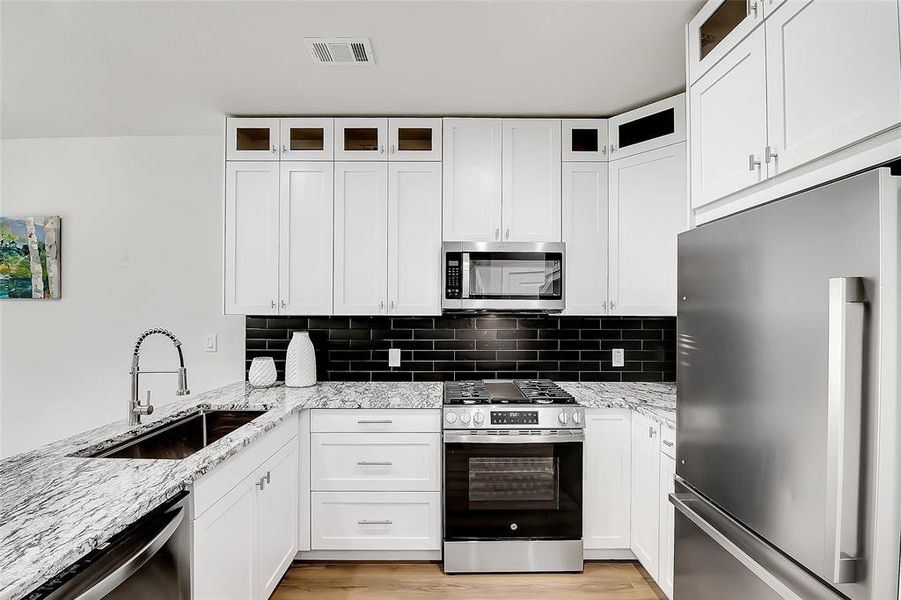 Kitchen with light wood-style floors, sink, stainless steel appliances, light granite countertops, and white custom cabinetry