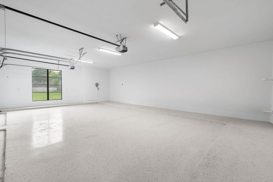 A spacious, pristine garage features bright overhead lighting and a single window offering a glimpse of the outdoors.