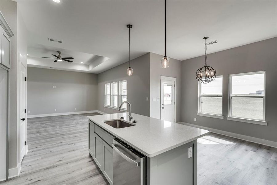 Kitchen featuring ceiling fan with notable chandelier, dishwasher, a center island with sink, sink, and light hardwood / wood-style floors