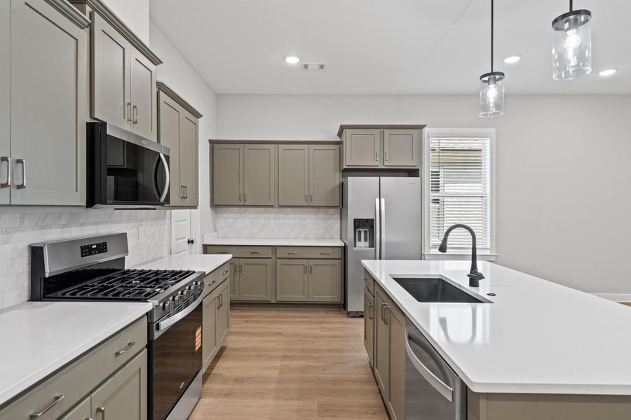 Kitchen with appliances with stainless steel finishes, pendant lighting, decorative backsplash, gray cabinets, and a center island with sink