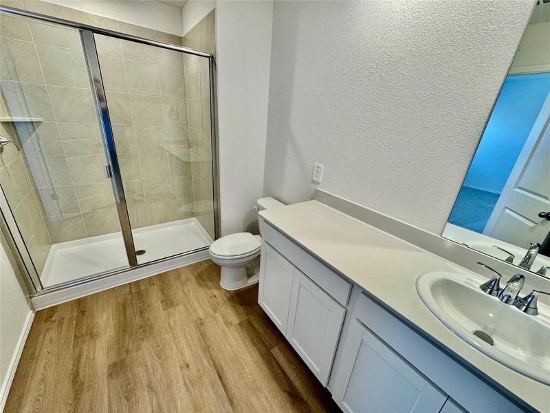 Bathroom with a stall shower, vanity, a textured wall, and light wood-style floors