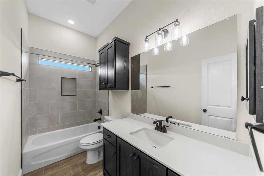 Bathroom featuring a white bathtub, tiled shower surround with a horizontal window, wood-finish flooring, dark wood cabinetry, and a large vanity mirror with overhead lighting
