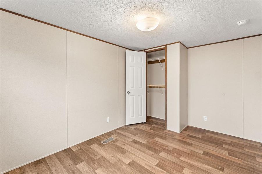 Unfurnished bedroom featuring light wood-style flooring, a textured ceiling, a closet, and crown molding