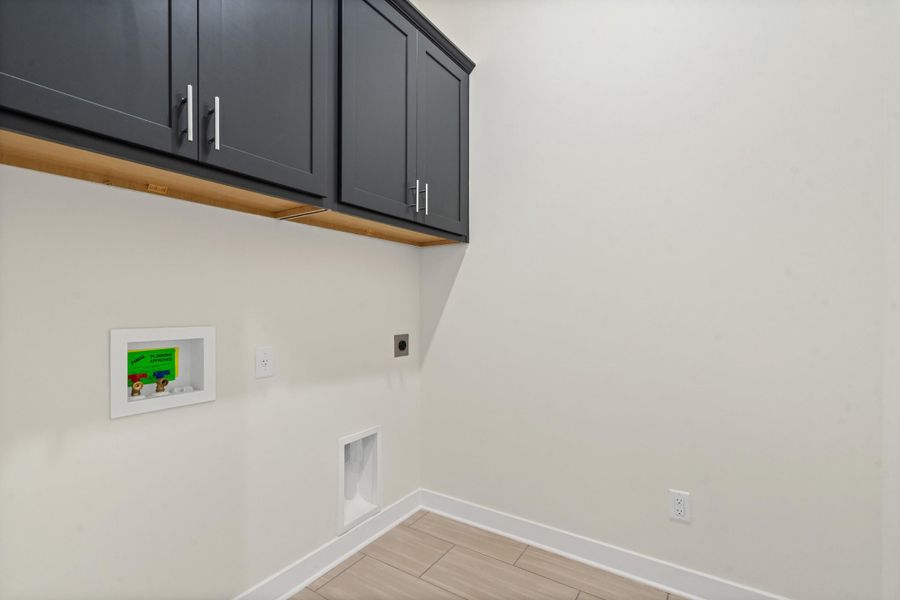Laundry area featuring dark cabinetry, light-toned wood-finish flooring, and crisp white walls Laundry area featuring dark cabinetry, light-toned wood-finish flooring, and crisp white walls