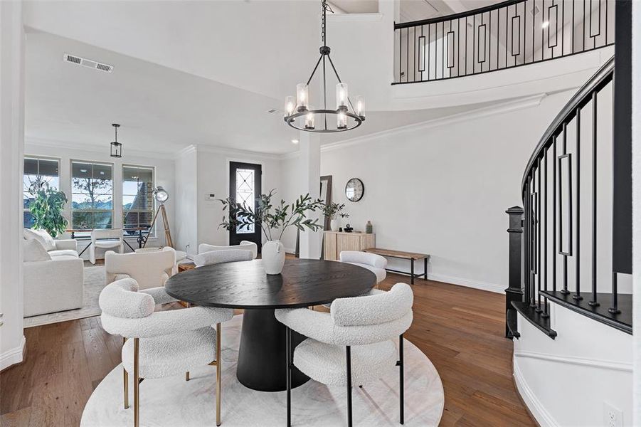 Dining area featuring crown molding, a notable chandelier, wood finished floors, visible vents, and stairway