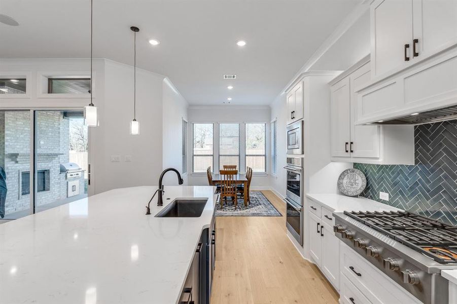 Kitchen featuring pendant lighting, white cabinets, sink, light stone countertops, and appliances with stainless steel finishes