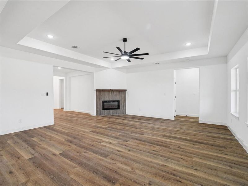 Unfurnished living room featuring a tiled fireplace, a tray ceiling, dark wood-style flooring, a ceiling fan, and recessed lighting