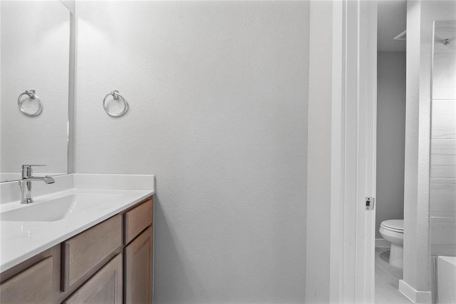 Secondary bath features a private vanity area and then opens to a shared tub/shower combo and toilet. Features include tile flooring, bath/shower combo with tile surround, wood stained cabinets, beautiful light countertops, mirror, dark, sleek fixtures and modern finishes!