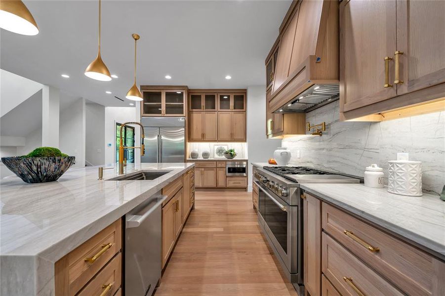 Kitchen featuring light stone countertops, high quality appliances, custom exhaust hood, decorative light fixtures, and tasteful backsplash Kitchen featuring light stone countertops, high quality appliances, custom exhaust hood, decorative light fixtures, and tasteful backsplash