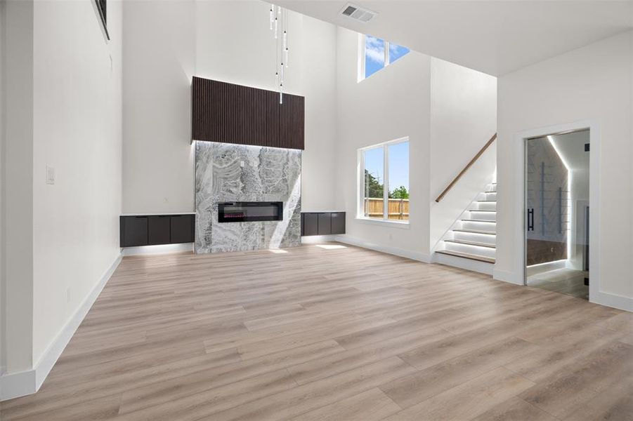 This spacious interior features light wood flooring, a fireplace with a natural stone surround, and high ceilings with an overhead light fixture This spacious interior features light wood flooring, a fireplace with a natural stone surround, and high ceilings with an overhead light fixture
