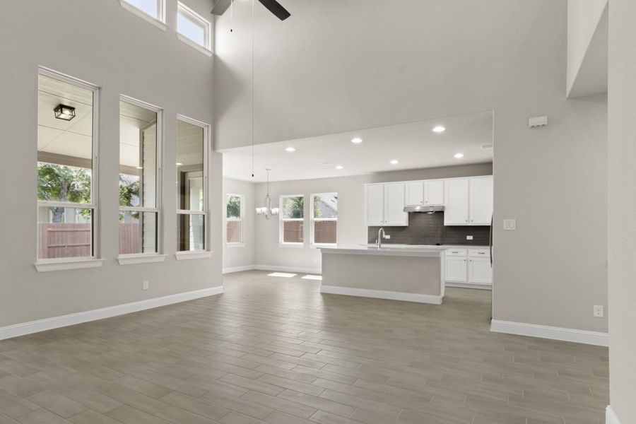Kitchen and living room with white countertops, white cabinets, steel appliances, and gray blacksplash tile, white painted walls and vinyl flooring.