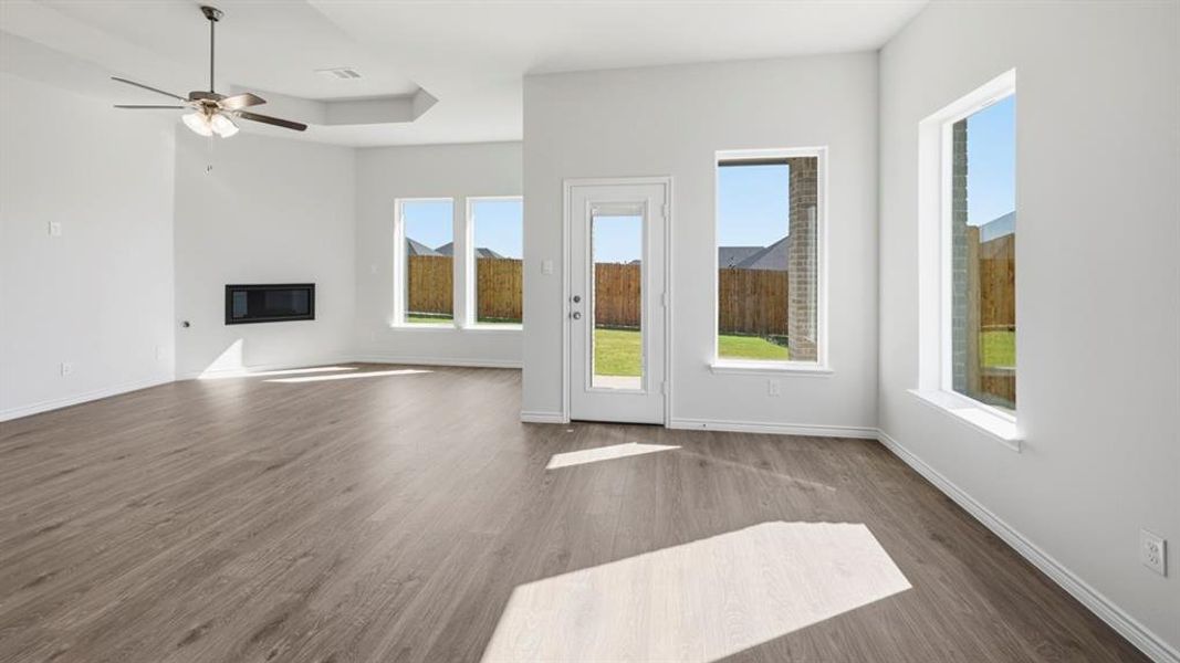 Open-concept living area featuring wood-finish flooring, a contemporary wall-mounted fireplace, and a tray ceiling with a ceiling fan
