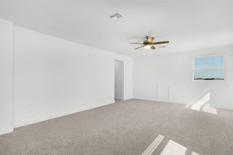 A well-lit room awaits your personal touch, featuring soft carpeting and a ceiling fan for comfort.