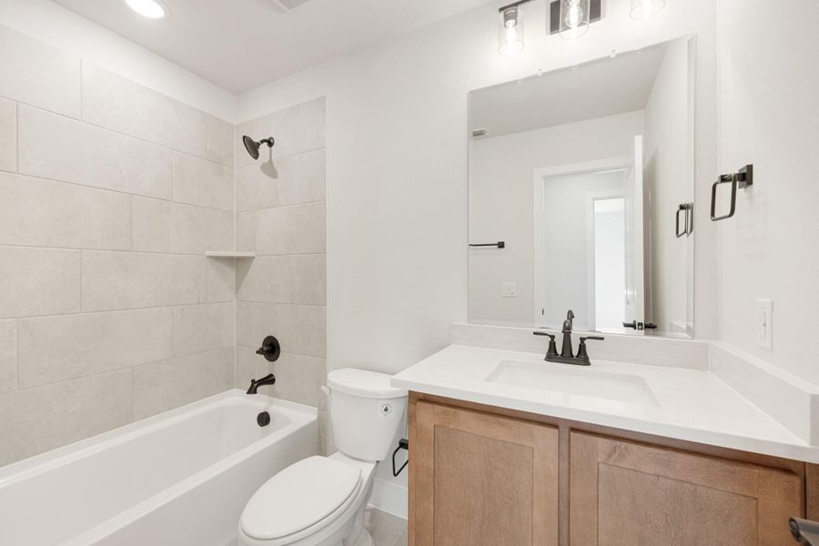 Bathroom with tiled tub-shower combo, wood vanity with white countertop, and dark bronze fixtures