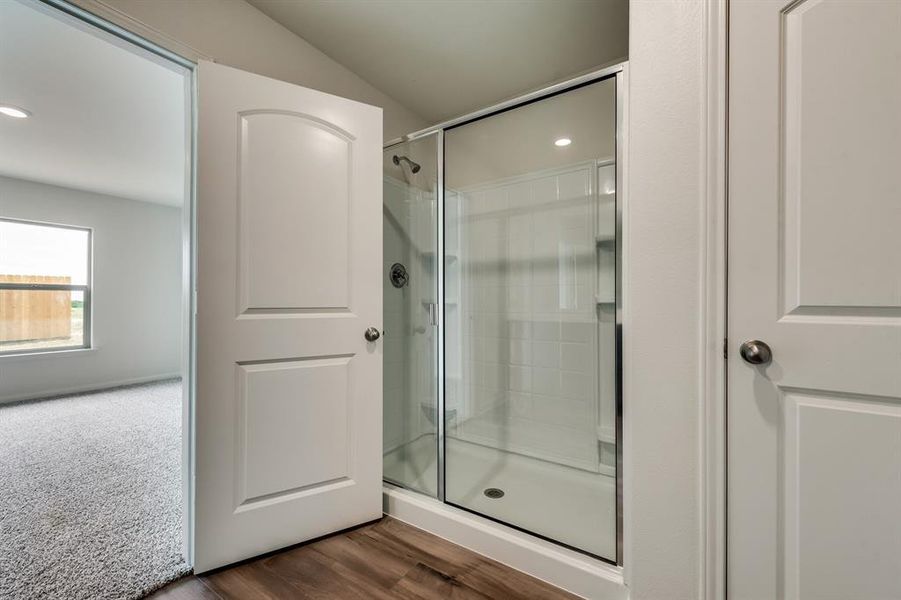 Bathroom with a shower with shower door, wood-type flooring, and vaulted ceiling