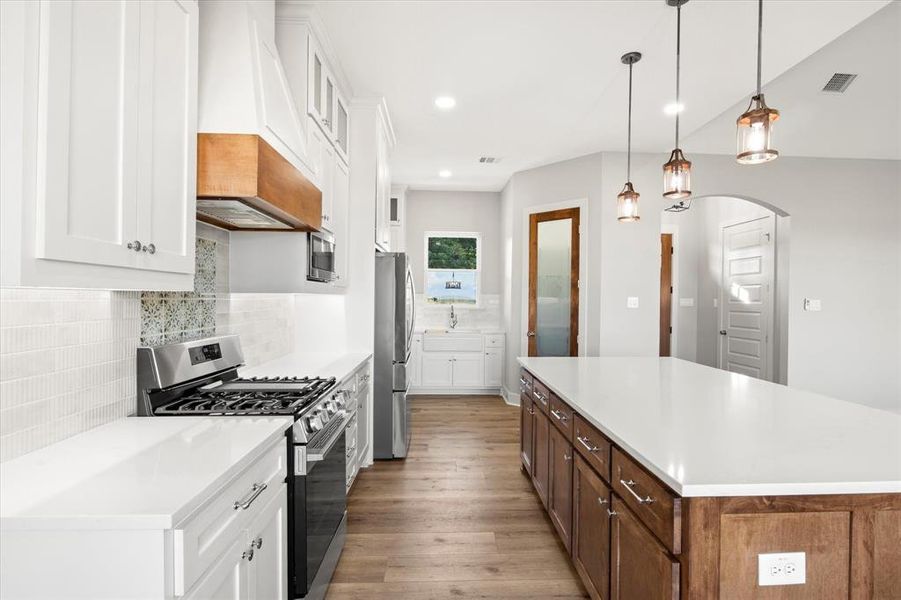 Kitchen with white cabinetry, stainless steel appliances, a kitchen island, backsplash, and recessed lighting Kitchen with white cabinetry, stainless steel appliances, a kitchen island, backsplash, and recessed lighting