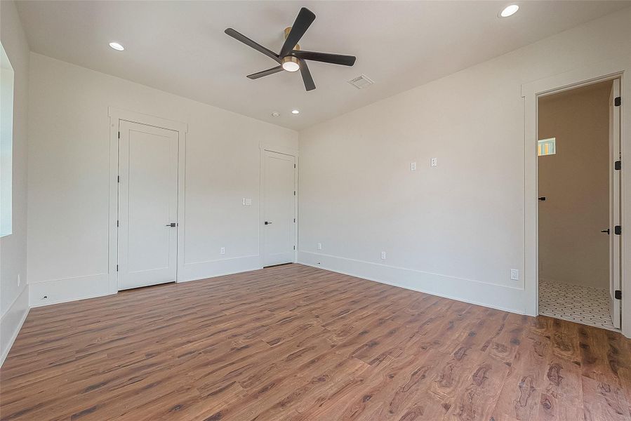 This is a bright, empty room with modern wood flooring, two white doors, and a ceiling fan. There's a third open door leading to a tiled area. The space offers a clean canvas for personalization. This is a bright, empty room with modern wood flooring, two white doors, and a ceiling fan. There's a third open door leading to a tiled area. The space offers a clean canvas for personalization.