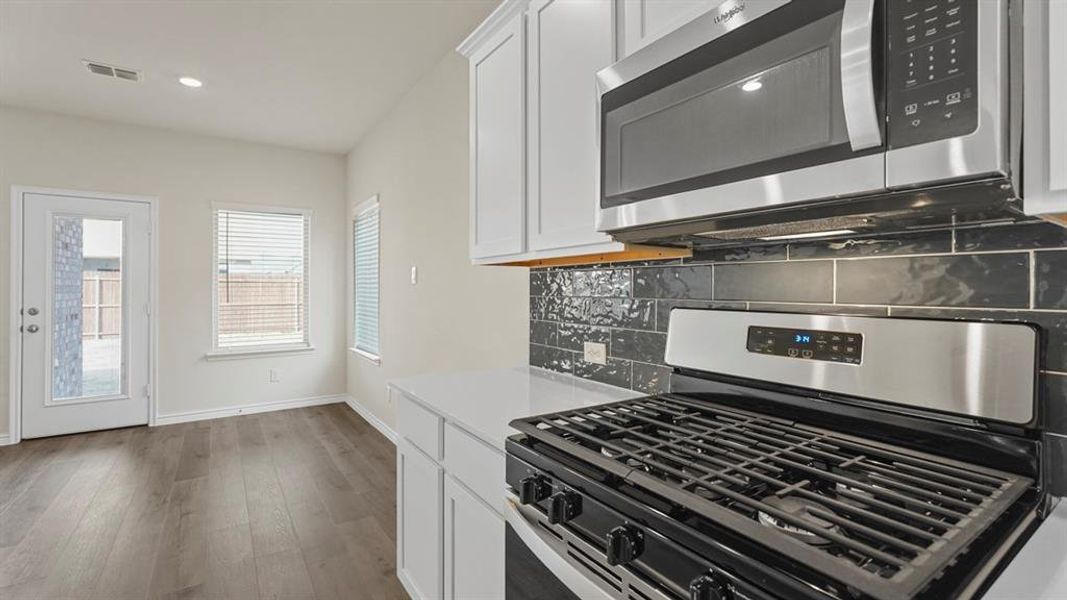 Modern kitchen featuring stainless steel appliances, crisp white cabinetry, a dark subway tile backsplash, light countertops, and wood-finish flooring