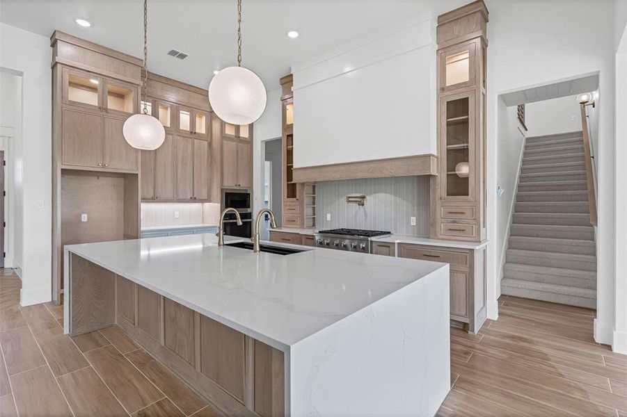 Kitchen featuring light stone counters, backsplash, wood finish floors, glass insert cabinets, and light brown cabinets Kitchen featuring light stone counters, backsplash, wood finish floors, glass insert cabinets, and light brown cabinets