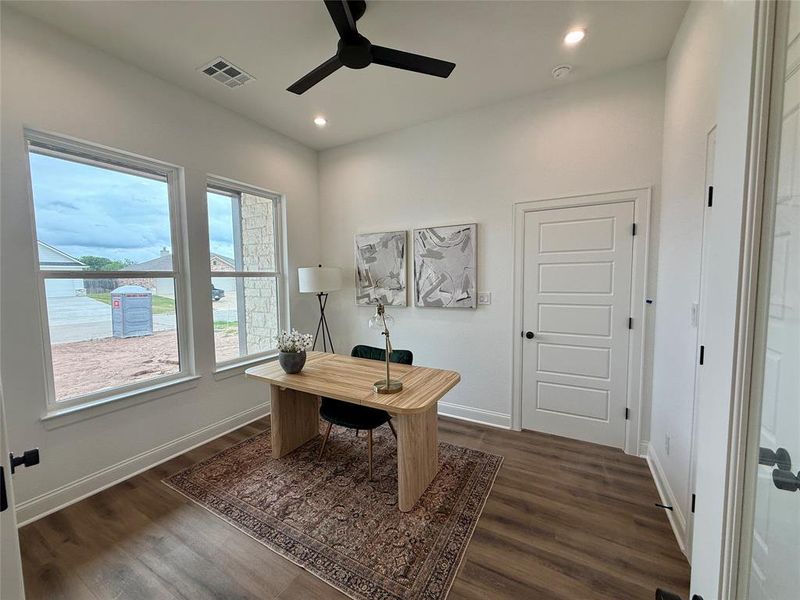 Spacious room featuring wood-finish flooring, two large windows, and a ceiling fan with integrated lighting