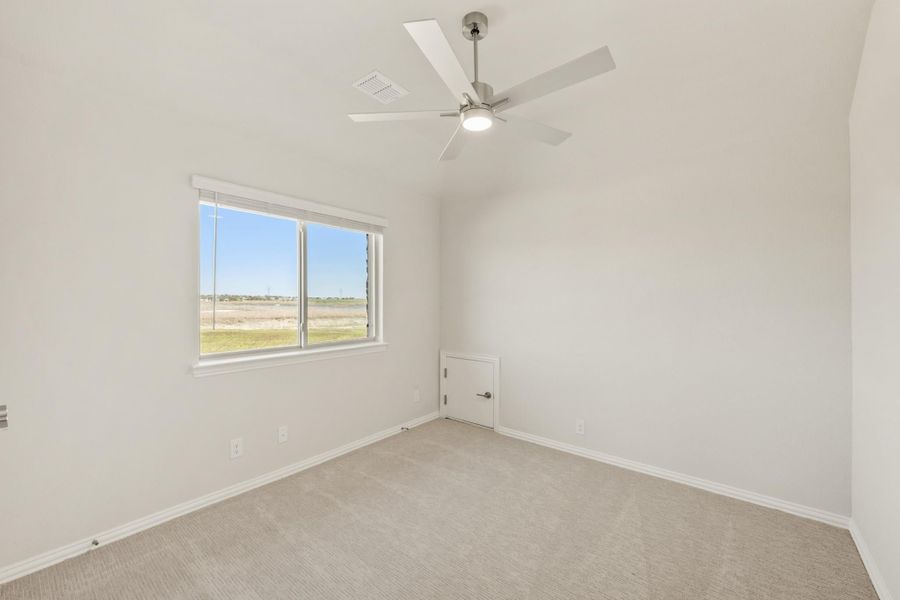 Empty bedroom with beige carpet, ceiling fan, and a window with outdoor views
