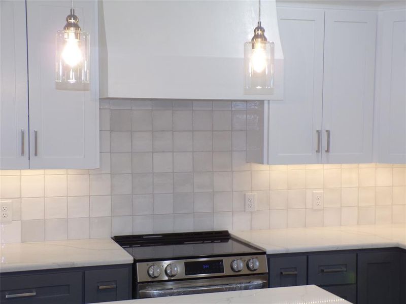 Kitchen with tasteful backsplash, hanging light fixtures, white cabinets, and electric range