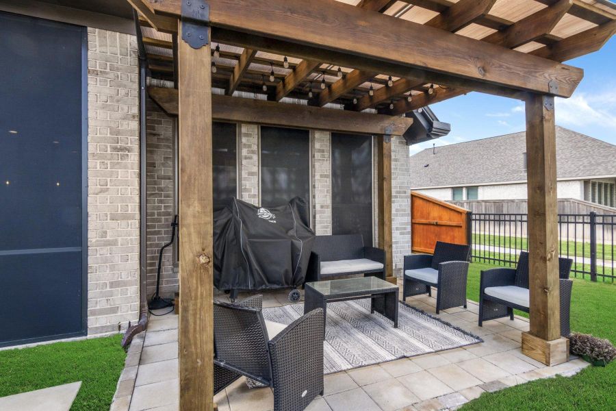 This photo showcases a cozy outdoor patio area with a wooden pergola. It features a combination of brick and stone flooring, creating a perfect space for entertaining or relaxing.
