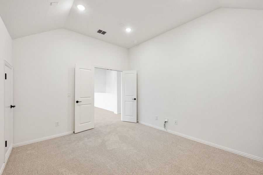 Empty bedroom with vaulted ceiling, carpet flooring, and two white doors with black hardware