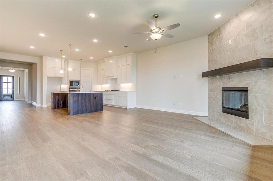 Unfurnished living room featuring sink, a fireplace, tile walls, light hardwood / wood-style floors, and ceiling fan