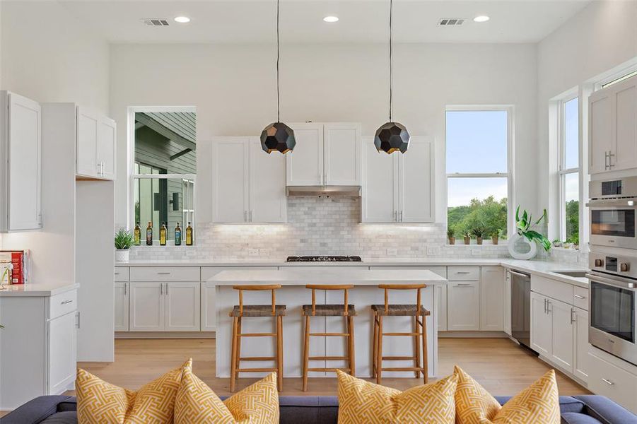 Kitchen featuring white cabinetry, a kitchen breakfast bar, light wood finished floors, stainless steel appliances, and tasteful backsplash