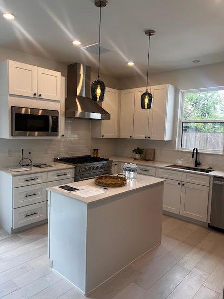 Kitchen featuring wall chimney range hood, stainless steel appliances, decorative backsplash, light countertops, and recessed lighting