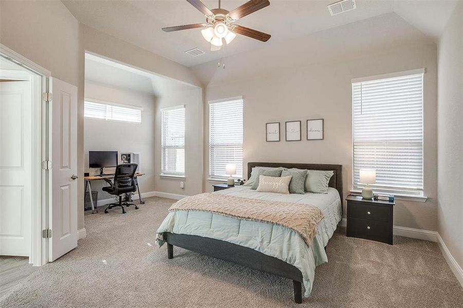 Carpeted primary bedroom with ceiling fan, seating area and natural light