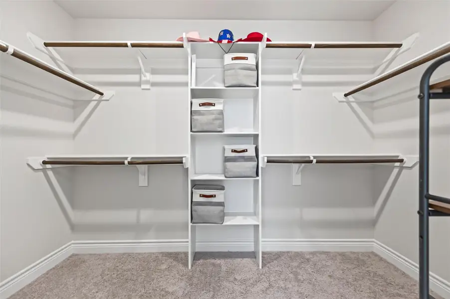 Spacious primary suite walk-in closet featuring extensive custom organization, including multiple high-capacity hanging garment racks, built-in shelving units, and dedicated storage space for apparel and accessories. Spacious primary suite walk-in closet featuring extensive custom organization, including multiple high-capacity hanging garment racks, built-in shelving units, and dedicated storage space for apparel and accessories.
