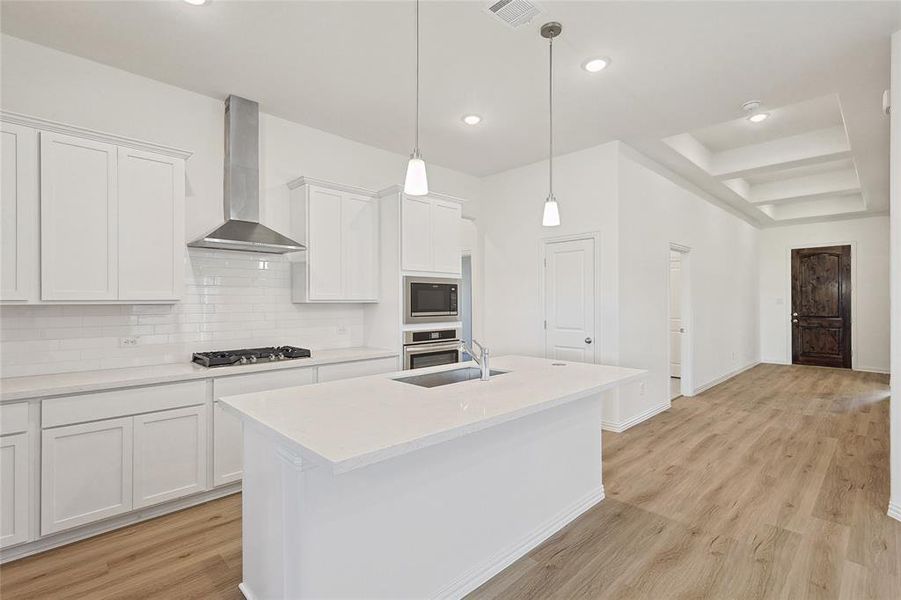 Kitchen with white cabinets, sink, wall chimney range hood, and stainless steel appliances