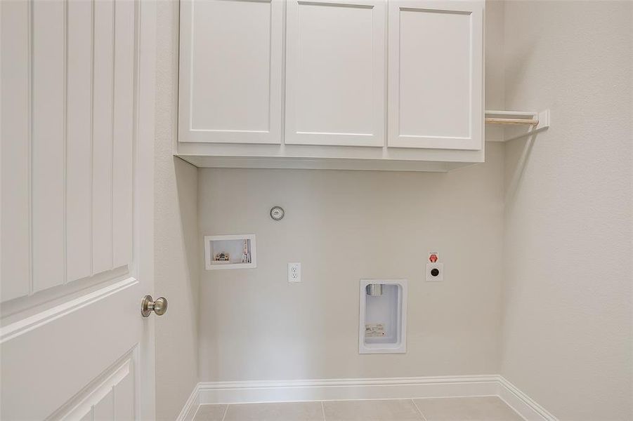 Clothes washing area featuring hookup for a washing machine, hookup for an electric dryer, light tile patterned flooring, gas dryer hookup, and cabinets