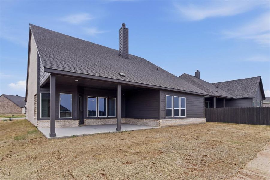 Back of property featuring a shingled roof, a patio, a chimney, and brick siding