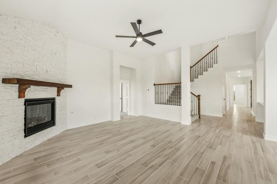 Open living room with white brick fireplace, wood mantel, ceiling fan, and staircase with iron balusters Open living room with white brick fireplace, wood mantel, ceiling fan, and staircase with iron balusters