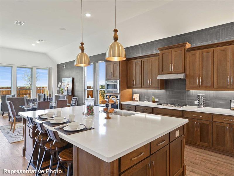 Kitchen with light wood-style flooring, lofted ceiling, pendant lighting, a kitchen bar, and decorative backsplash Kitchen with light wood-style flooring, lofted ceiling, pendant lighting, a kitchen bar, and decorative backsplash