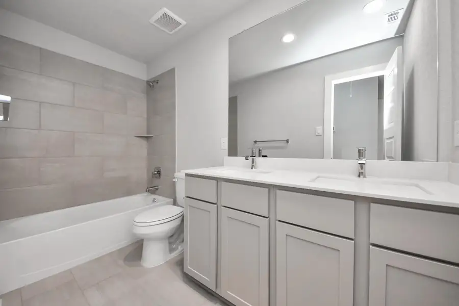 Secondary bath features tile flooring, bath/shower combo with tile surround, light stained wood cabinets, beautiful light countertop. Sample photo of completed home with similar floor plan. Actual colors and selections may vary.