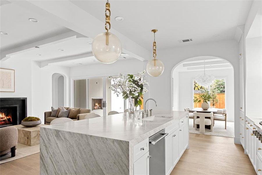 Kitchen featuring a lit fireplace, arched walkways, hanging light fixtures, an island with sink, and recessed lighting