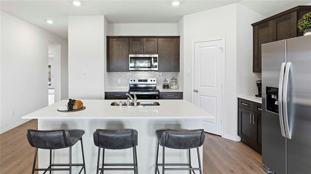 Kitchen featuring stainless steel appliances, dark wood finish cabinets, an island with sink, decorative backsplash, and recessed lighting