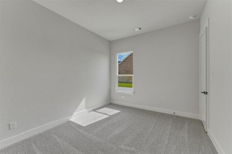 Light gray wall paint, gray carpet flooring, white trim, a single window, and a white door with black hardware Light gray wall paint, gray carpet flooring, white trim, a single window, and a white door with black hardware