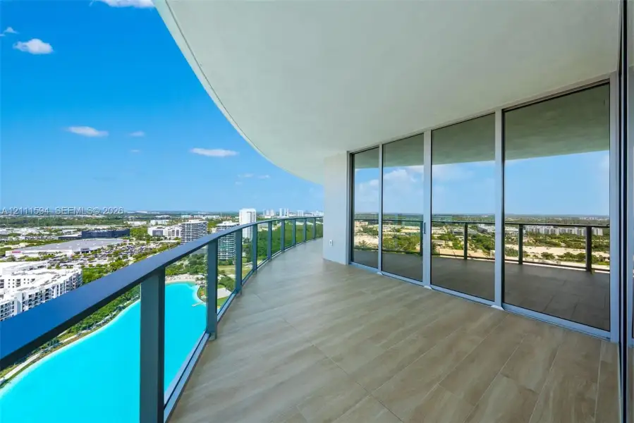 Expansive covered balcony featuring tile flooring, metal railing, and floor-to-ceiling glass panel doors Expansive covered balcony featuring tile flooring, metal railing, and floor-to-ceiling glass panel doors