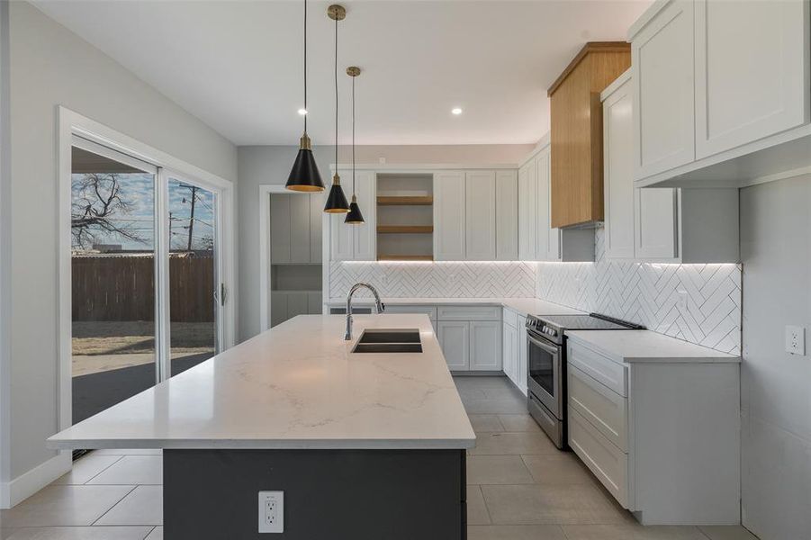 Kitchen featuring an island with sink, hanging light fixtures, white cabinetry, stainless steel range oven, and light stone countertops